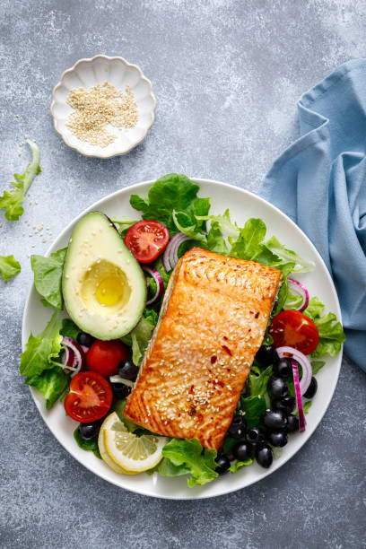 filete de pescado de salmón a la plancha y ensalada de verduras frescas con tomate, cebolla roja, aceitunas negras y aguacate - mediteranean cuisine fotografías e imágenes de stock