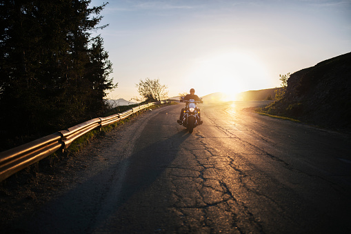 Motorist driving motorcycle on sunset.