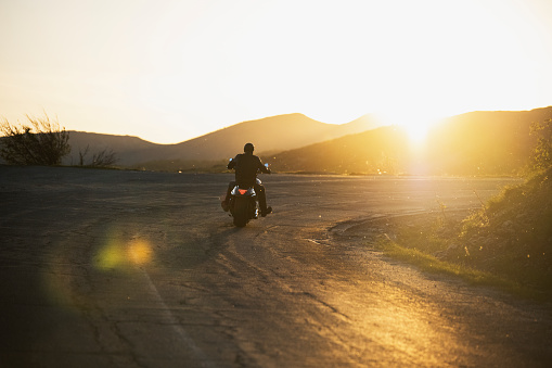 Biker riding motorcycle on mountain road on sunset.