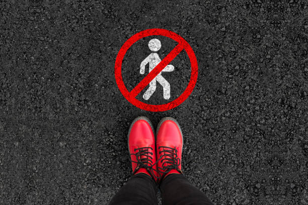 woman legs in boots standing on asphalt road and No walking sign