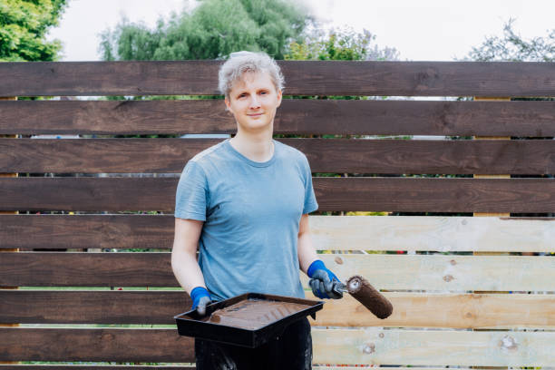 ritratto di giovane lavoratore dipinge con un rullo una recinzione di legno in giardino. fai da te, concetto fai da te. miglioramento della casa. ristrutturazione e ristrutturazione della casa. messa a fuoco selettiva, spazio di copia. - paint roller copy space action adult foto e immagini stock