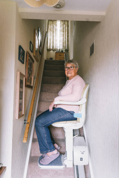 starsza kobieta korzystająca z automatycznej windy schodowej na klatce schodowej w swoim domu. medyczna winda schodowa dla osób niepełnosprawnych i starszych w domu. karta pionowa. selektywne ustawianie ostrości. - power chair zdjęcia i obrazy z banku zdjęć