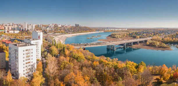 Photo of Aerial cityscape view of city districts with automobile bridge over river in Ufa. Autumn parks with colorful trees