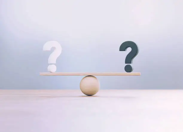 Photo of White And Black Question Marks Sitting Over Wooden Seesaw Scale Before Defocused Background