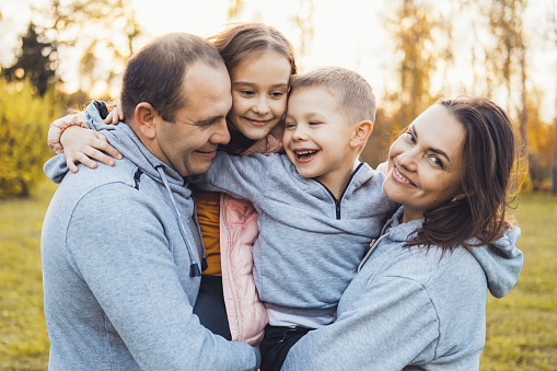 Portrait of happy family of four posing in park in autumn, mom and dad carrying their two laughing kids in arms playing, having fun together. Smiling happy child. Family day. Activity relationship.