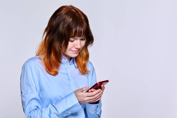 istock Smiling teenage female looking at smartphone screen, on light studio background, copy space 1399348380