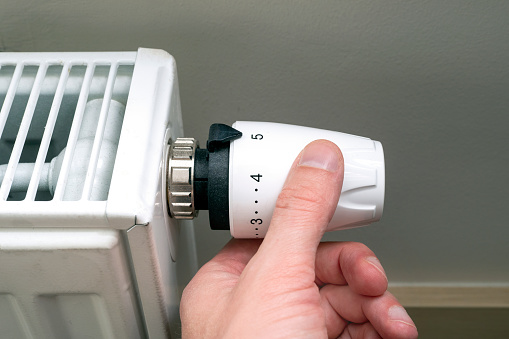 Man regulating heating temperature with a modern wireless thermostat installed on the wall at home.