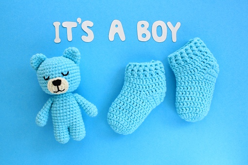It's a boy lettering, crochet bear and baby booties on blue background. Baby boy birth, new life, family concept. Greeting card idea for newborn. Pregnancy announcement. Flatlay, top view