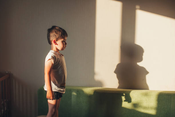 istock Profile of a boy standing on the couch staring at his shadow on the wall. Having cute face. Standing against room interior. 1399349742