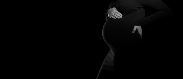 Panorama of side view of pregnant woman in black dress on black background