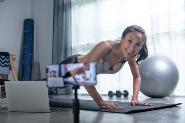 ライブストリーミングに携帯電話のカメラを使用しているアジアの女性は、リビングルームでオンラインでヨガを教えています。 - living room learning healthy lifestyle one person ストックフォトと画像
