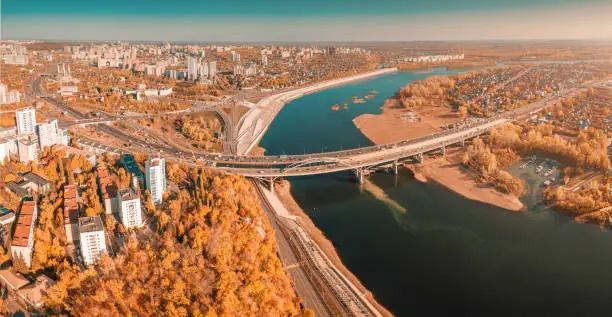 Photo of Aerial cityscape view of city districts with automobile bridge over river in Ufa. Autumn parks with colorful trees