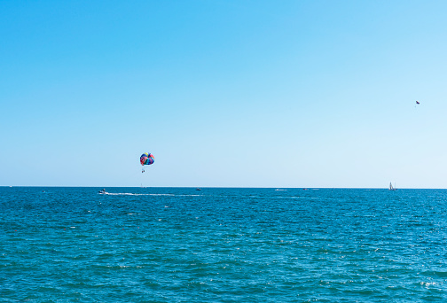 parasailing multicolored rainbow parachute behind boat over blue turquoise sea landscape summer activities copy space selective focus