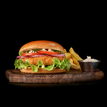Delicious fastfood fresh tasty burger. crispy, breaded chicken burger with and vegetable and french fries on wooden tray, isolated on dark background