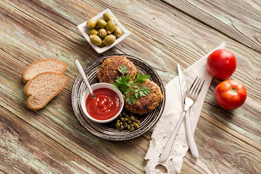 Cutlets with minced meat and rice, tomato sauce, olives on a wooden table close-up