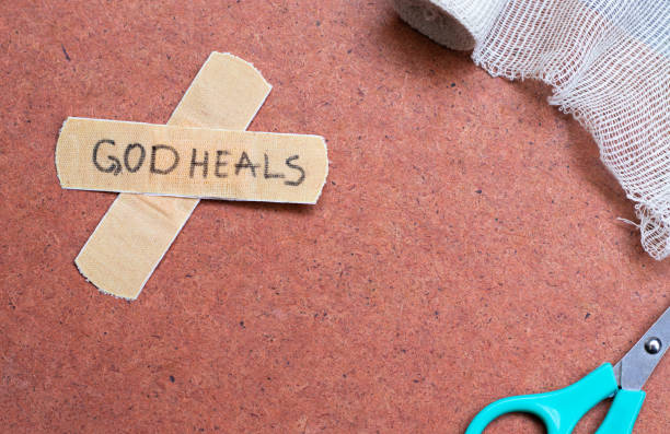 God heals a handwritten text note on a bandage tape with a medical bandage and scissors on a textured background with copy space stock photo