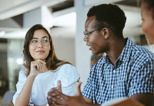 istock Three young happy businesspeople having a meeting while sitting at a table at work. Business professionals talking and planning in an office together. African american man discussing a business strategy with coworkers 1399362820