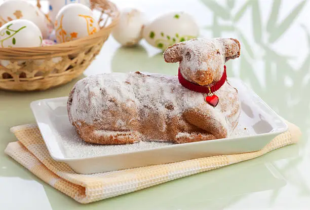 traditional easter lamb cake with powdered sugar, basket full of easter eggs in background