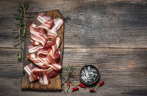 Raw bacon with different spices on a cutting board on a rustic wooden board