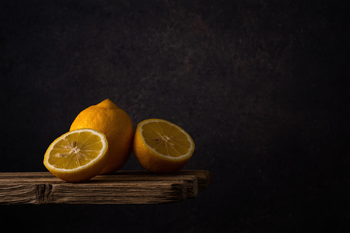 whole and halves of a fresh ripe lemon lie in a group on old boards on a dark soft backdrop. side view. moody artistic photo with copy space
