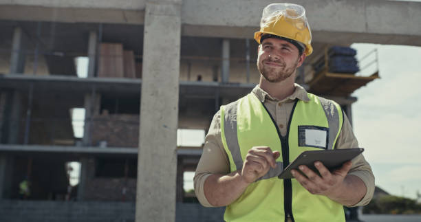 A building contractor using a digital tablet while working on a construction site. A young man browsing online with a smart device while working on an architecture project stock photo