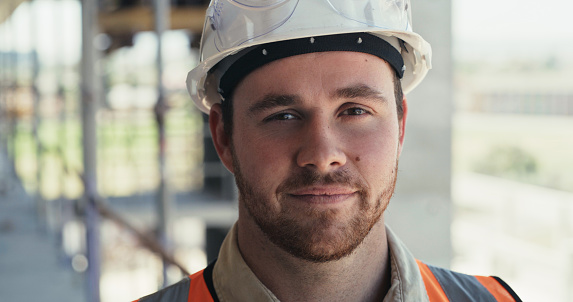 Portrait of a building contractor working on a construction site. Face of a young man working on an architecture project, looking at the camera