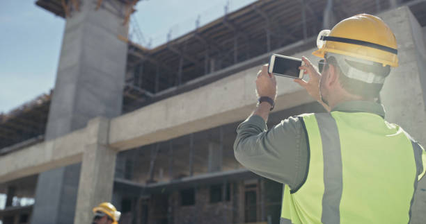 A building contractor taking photos on a phone while working on a construction site. A man using a smartphone while working on an architecture project A building contractor taking photos on a phone while working on a construction site. A man using a smartphone while working on an architecture project architect photos stock pictures, royalty-free photos & images