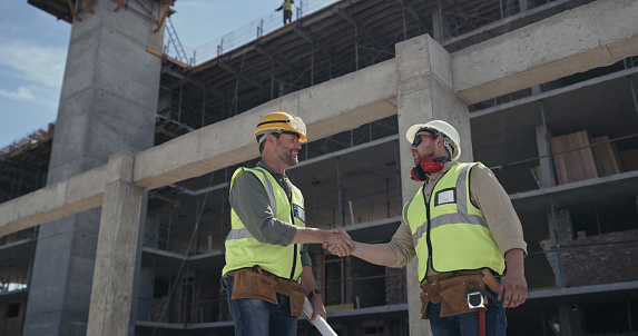 Builders making a deal with a handshake at a construction site. Two men working as a team on an architecture project. Engineers and colleagues shaking hands