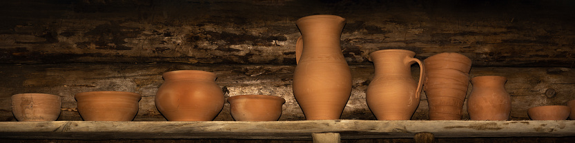 earthenware stands in a row on a rough plank shelf against a log wall. large-format still life in a simple rustic style. pottery shop