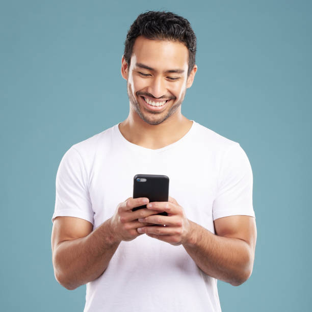 istock Handsome young mixed race man using his phone while standing in studio isolated against a blue background. Hispanic male sending a text message, using the internet online or browsing social media 1399365617
