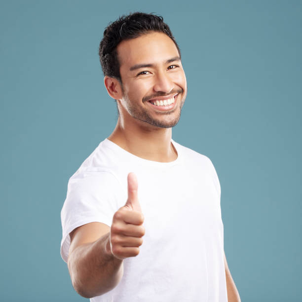 istock Handsome young mixed race man giving thumbs up while standing in studio isolated against a blue background. Hispanic male showing support or appreciation. Backing or endorsing a product or company 1399365913
