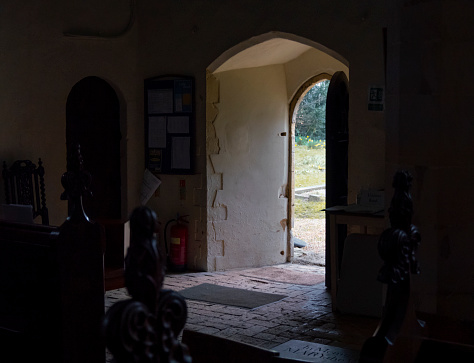 The dark interior of a small church in rural England with spring sunlight outside.