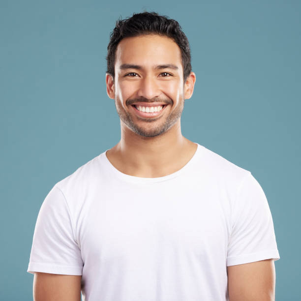 Handsome young mixed race man smiling and happy while standing in studio isolated against a blue background. Hispanic male in casual wear expressing happiness with a smile and looking at the camera Handsome young mixed race man smiling and happy while standing in studio isolated against a blue background. Hispanic male in casual wear expressing happiness with a smile and looking at the camera hair stubble stock pictures, royalty-free photos & images