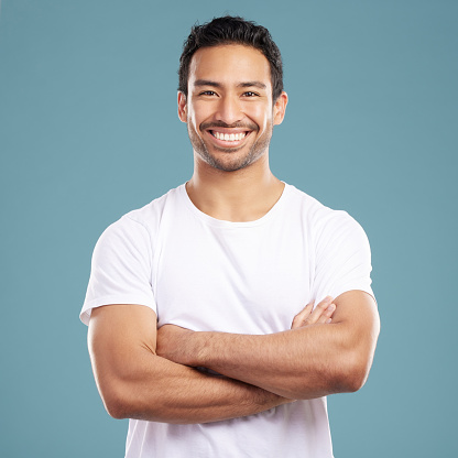 Handsome young mixed race man with his arms crossed while standing in studio isolated against a blue background. Happy hispanic male smiling while looking confident and powerful with his arms folded