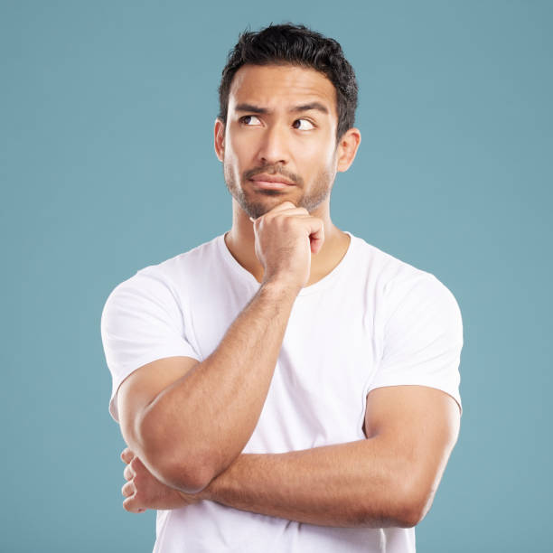 istock Handsome young mixed race man looking thoughtful with his hand on his chin and looking away while standing in studio isolated against a blue background. Hispanic male thinking about a bright idea 1399366152