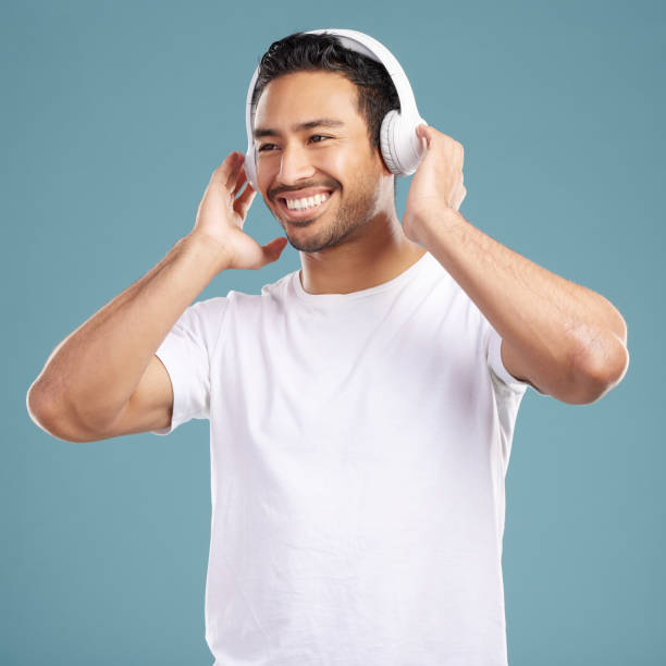 istock Handsome young mixed race man listening to music while standing in studio isolated against a blue background. Hispanic male streaming his favourite playlist online using wireless headphones 1399366157