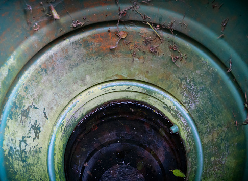 The view inside a dirty plastic water butt, with a small amount of filthy water in the bottom and dead leaves and grass encrusting the rim.