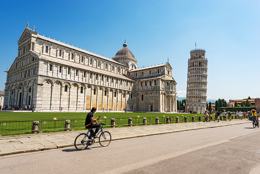 Pisa, Italy - July 29, 2020: Cathedral (Duomo of Santa Maria Assunta) and the Leaning Tower of Pisa, Piazza dei Miracoli (Square of Miracles), UNESCO world heritage site, Tuscany, Italy, Europe. A large group of tourists visit the famous monuments on a sunny summer day.
