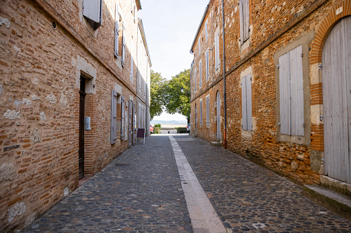 A wide-angle view of an empty cobbled street in the small town of Auvillar in Toulouse in the South of France. There is an idyllic view in the distance.