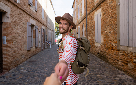 A point of view of a male traveler in a fedora holding her partner's hand as they travel in the streets of Auvillar in Toulouse in the South of France.