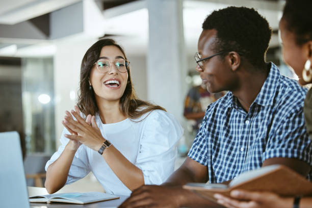 istock Three young happy businesspeople having a meeting while sitting at a table and working on a laptop at work. Business professionals talking and planning in an office together. Hispanic woman discussing a business strategy with coworkers 1399370914