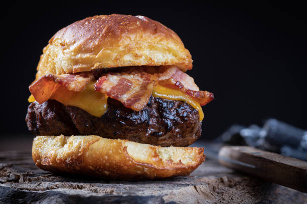 Bacon cheeseburger on a toasted bun Closeup of a bacon cheeseburger on toasted bun on a rustic wooden board against a black backgound with copy space bacon cheeseburger stock pictures, royalty-free photos & images