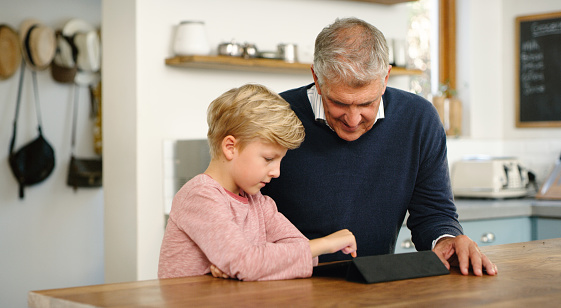 Family using tablet at home. A senior man and little boy learning online with digital technology. Grandfather and cute grandson playing with a touchscreen