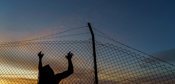 Refugee man climbing to the fences at dawn