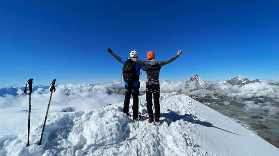 Magnificent view of a person on a snow-covered mountain summit of Breithorn in Switzerland. Celebrating a success. Looking down from the top with arms spread. Taking in the view in an embrace