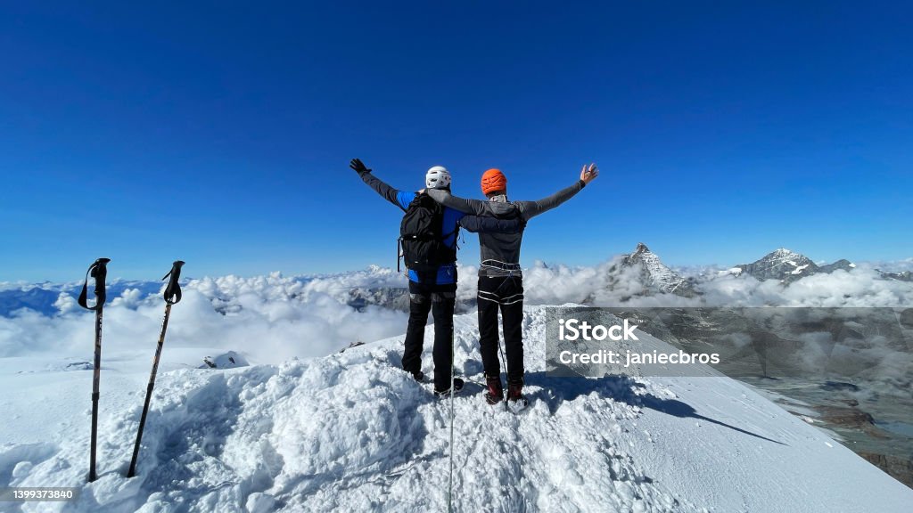 Breithorn in Switzerland Summit. Magnificent view of a person on a snow-covered mountain summit of Breithorn in Switzerland. Celebrating a success. Looking down from the top with arms spread. Taking in the view in an embrace Mountain Climbing Stock Photo