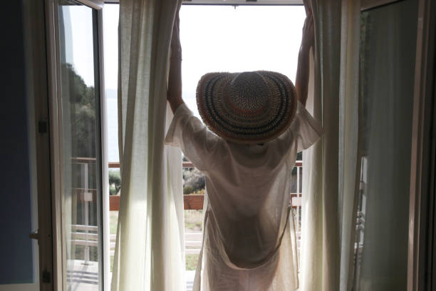 istock Back view of a woman looking outdoors through a window and opening curtains 1399375295