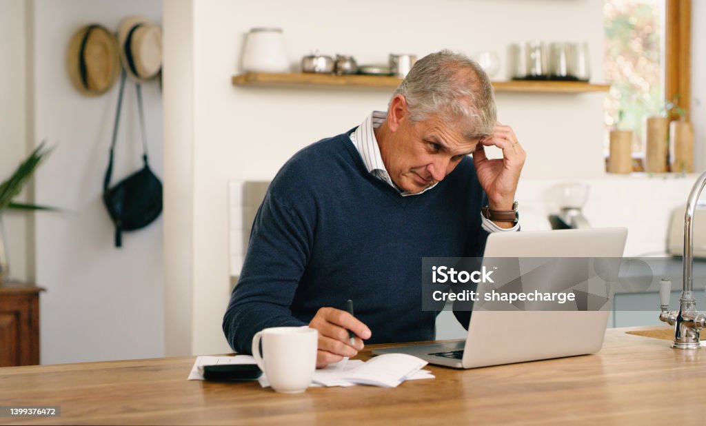 A senior man planning his finance, paying bills and looking unhappy while using laptop at home. A mature man going through paperwork and working online with a computer and feeling confused, stressed and unsure Mistake Stock Photo