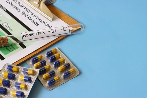 Stock photo showing close-up, elevated view of lab test labelled glass test tube on completed medical form for Monkeypox (Poxviridae) virus test.