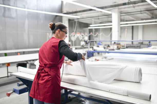 vista trasera de una trabajadora textil experta que desenrolla rollos de material para cortar - embroidery textile industry clothing factory fotografías e imágenes de stock